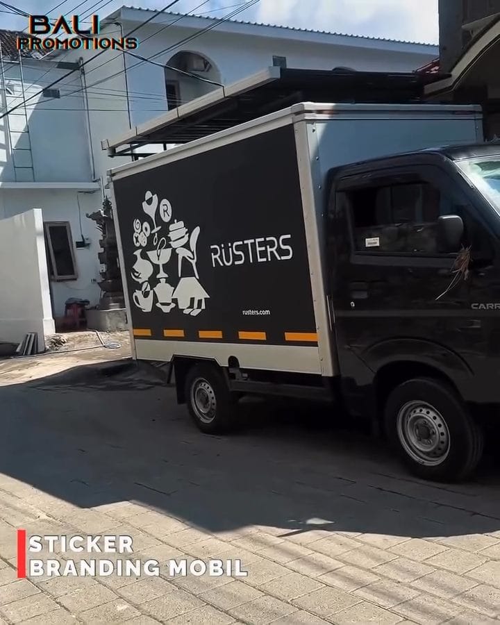 3 Manfaat Wrapping Mobil Box untuk Promosi Bisnis Bali Hasil wrapping mobil box berwarna hitam matte dengan desain minimalis putih di jalanan kota Bali.